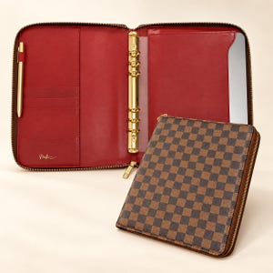 May include: A zippered planner binder with a brown and black checkered exterior and a red interior. The interior features a gold six-ring mechanism, multiple card slots, a pen loop with a gold pen, and the brand name Neesha printed in gold.