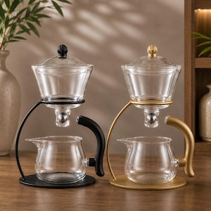 Puede incluir: Dos juegos de té de cristal sobre soportes. Un juego cuenta con soporte, asa y remate de tapa de metal negro mate. El otro juego cuenta con soporte, asa y remate de tapa de metal dorado mate. Cada juego incluye un gotero y una jarra de cristal.