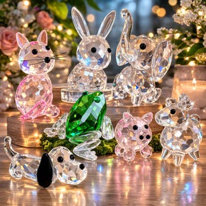 以下が含まれることがあります： ピンクの猫、透明なウサギ、ゾウ、緑のカエル、ピンクの豚、ヒツジ、黒い耳の犬など、面カットされたクリスタル動物の置物のコレクション。 木の表面に置かれた置物です。