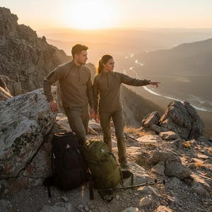 Peut inclure: Deux personnes vêtues de vêtements de plein air vert olive se tiennent sur un sommet rocheux, avec deux sacs à dos et des bâtons de randonnée à proximité. Les vêtements comprennent des chemises à manches longues et des pantalons. L'arrière-plan présente des montagnes et une rivière au coucher du soleil.