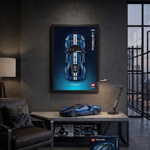 May include: A framed wall poster featuring a top-down view of a blue Ford GT model car with white racing stripes, accompanied by the text Ford GT and the LEGO logo. Below, a blue Ford GT model car sits on a table next to a LEGO Technic box.