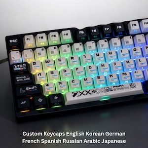 Puede incluir: Un teclado mecánico negro con teclas personalizadas. Las teclas son blancas con letras negras y tienen retroiluminación arcoíris. La imagen incluye el texto "Custom Keycaps English Korean German French Spanish Russian Arabic Japanese."