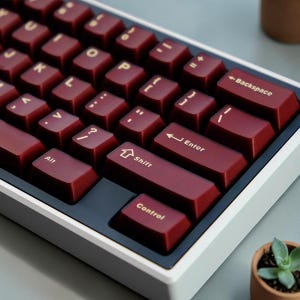 Könnte beinhalten: Eine weiße Keramik-Tasse mit schwarzem Henkel und dem Text "But First, Coffee" in fetter, schwarzer Schrift. Die Tasse steht vor einem neutralen Hintergrund, der ihr schlichtes Design hervorhebt.