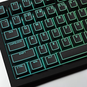 Puede incluir: Primer plano de un teclado mecánico negro con retroiluminación verde azulado. Las teclas están etiquetadas con letras y símbolos blancos. El teclado incluye teclas de función, una tecla de tabulación, una tecla de bloqueo de mayúsculas, shift, control, alt y win.
