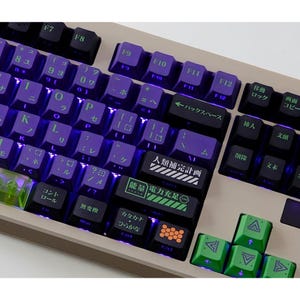 Op de afbeelding: Mechanisch toetsenbord met paarse en groene toetsen. De toetsen zijn gerangschikt in een standaard lay-out met Japanse tekens en Engelse letters. Sommige toetsen hebben Japanse tekst en het toetsenbord heeft een beige frame.