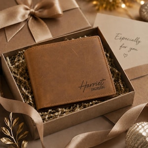 May include: A brown leather bifold wallet with the name Harriet Jackson engraved on the front, presented in a gift box filled with paper shred. A card inside the box features the text Especially for you with a small heart symbol below it.
