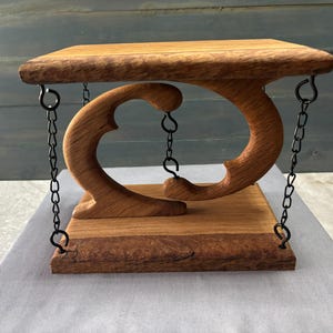 May include: A tensegrity sculpture featuring two carved wooden pieces connected by black metal chains. The top and bottom wooden platforms are held in suspension by the tension of the chains, creating a floating effect between the two curved shapes.