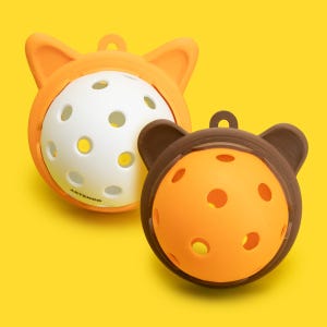 以下が含まれることがあります： 動物の耳の形をした突起と円形の穴がある2つの球体ペット用おもちゃ。1つはオレンジ色で中央が白、もう1つはダークブラウンで中央がオレンジ色。白い球体にはARTENGOという文字がプリントされています。