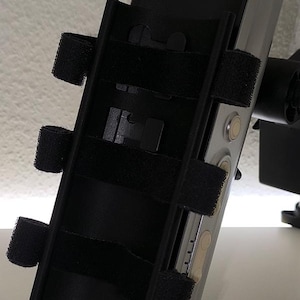 Könnte beinhalten: Ein schwarzes und silbernes Gerät mit verstellbaren Riemen und dem Aufdruck "LOVENER". Das Gerät hat mehrere schwarze Klettbänder und einen silbernen Körper mit mehreren kreisförmigen Knöpfen. Es scheint sich um eine Halterung oder Halterung zu handeln.