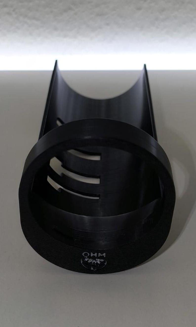 May include: A black cylindrical object with a rounded top and a circular base. The base has the letters "OHM" printed on it. The cylinder has several horizontal cutouts. The object is made of a matte black material.