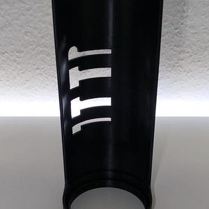 May include: A black cylindrical object with the letters "111" cut out of the side. The object has a circular base and a smooth, matte finish. The background is a plain white surface.