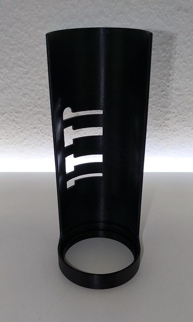 May include: A black cylindrical object with the letters "111" cut out of the side. The object has a circular base and a smooth, matte finish. The background is a plain white surface.