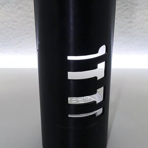 May include: A black cylindrical candle holder with a curved top. The holder has rectangular cutouts that allow light to pass through. The design is modern and minimalist, suitable for home decor.