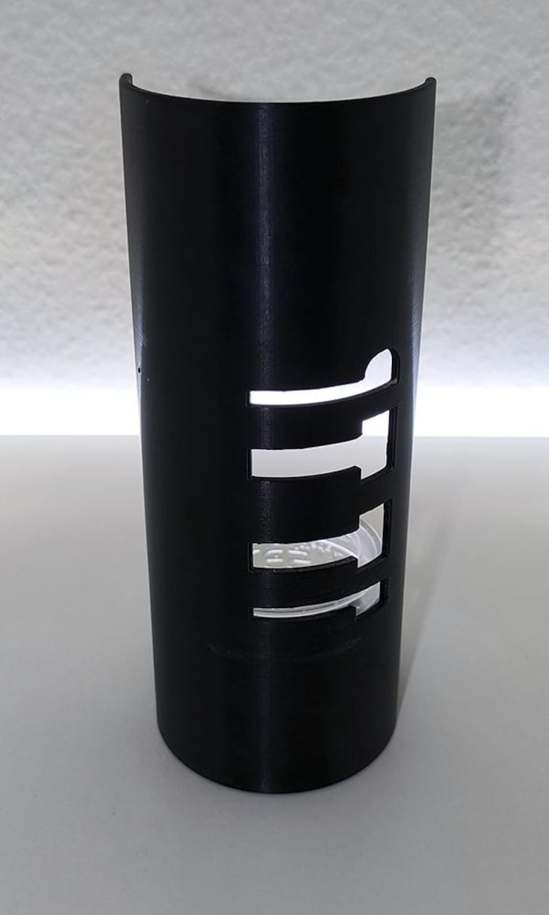 May include: A black cylindrical candle holder with a curved top. The holder has rectangular cutouts that allow light to pass through. The design is modern and minimalist, suitable for home decor.