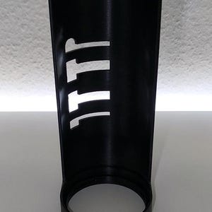 May include: A black, cylindrical container with a circular base. The side of the container has a series of white, vertical cutouts forming the letters "111". The object is made of a matte material.