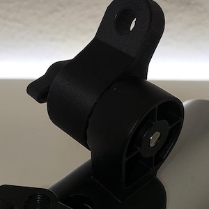 Könnte beinhalten: Schwarze Kamerahalterung mit rundem Loch und Knopf. Die Halterung besteht aus Kunststoff und hat ein Drehgelenk. Sie ist für die Befestigung an einer Stange oder einer anderen Tragstruktur konzipiert.