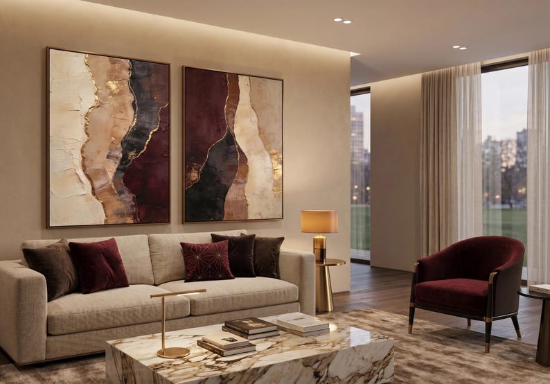 May include: Two large rectangular wall art pieces featuring abstract layers of cream, deep burgundy, black, and metallic gold paint. The textured canvases are displayed side-by-side, showcasing organic, flowing shapes and bold color contrasts.