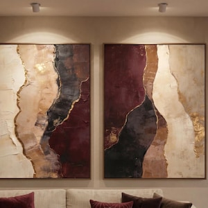May include: A set of two rectangular wall art canvases featuring abstract vertical bands of color. The palette includes deep burgundy, charcoal black, cream, and beige, with textured gold leaf accents separating the distinct color sections.