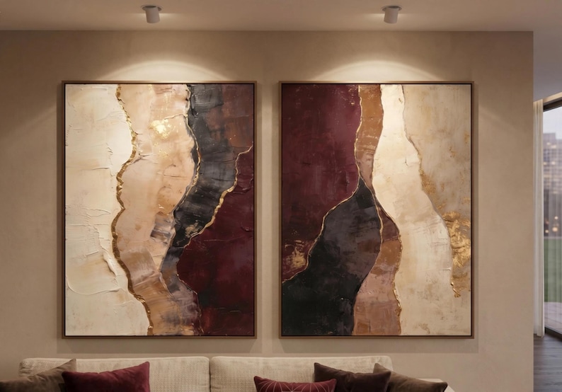 May include: A set of two rectangular wall art canvases featuring abstract vertical bands of color. The palette includes deep burgundy, charcoal black, cream, and beige, with textured gold leaf accents separating the distinct color sections.