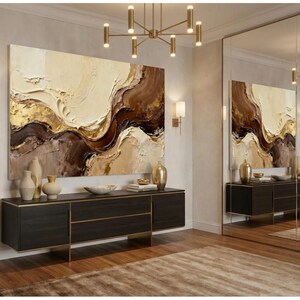 May include: An abstract painting in brown, beige, and gold tones hangs above a dark wood cabinet with gold trim. The cabinet displays vases and bowls. The artwork is reflected in a large mirror, creating a sense of space.