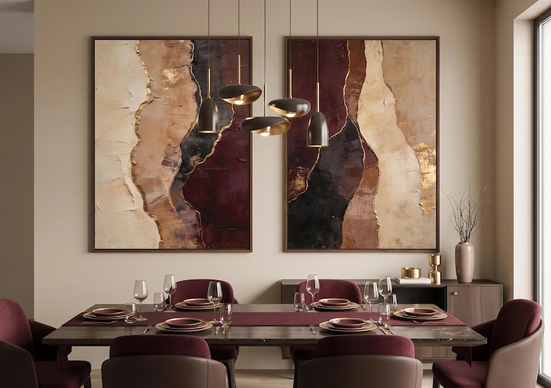 May include: Two large rectangular abstract paintings featuring layered textures in shades of cream, beige, deep burgundy, and black with gold leaf accents, displayed above a dining table set with burgundy chairs and a dark wood table.