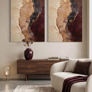 May include: Two rectangular wall art canvases featuring abstract layers of cream, beige, dark brown, and deep burgundy paint with textured gold leaf accents. The paintings display a vertical, flowing composition with thick, visible brushstrokes.