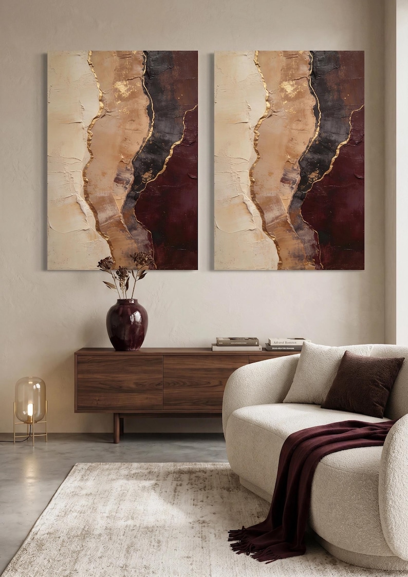 May include: Two rectangular wall art canvases featuring abstract layers of cream, beige, dark brown, and deep burgundy paint with textured gold leaf accents. The paintings display a vertical, flowing composition with thick, visible brushstrokes.