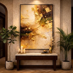 Peut inclure: Une peinture abstraite avec des accents de feuilles d'or est suspendue au-dessus d'une console en bois foncé. L'œuvre présente des couches texturées de crème, de marron et d'or. Des plantes en pot et des bougies flanquent la console.