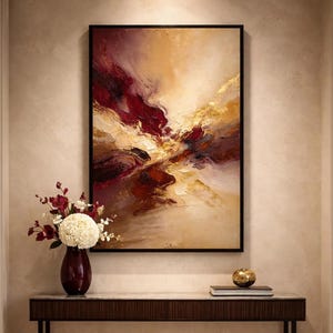 Peut inclure: Peinture à l'huile abstraite dans un cadre noir. L'œuvre présente un mélange de teintes bordeaux, dorées et beiges, créant une composition dynamique et texturée. Un vase rouge foncé avec des fleurs blanches et rouges est posé sur une table en bois foncé.
