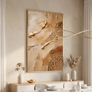 Könnte beinhalten: Abstrakte strukturierte Wandkunst in einem goldenen Rahmen. Das Kunstwerk zeigt ein mehrschichtiges Design mit Beige-, Braun- und Goldtönen. Das Design beinhaltet ein kreisförmiges Muster mit geometrischen Formen. Das Kunstwerk wird in einem gut beleuchteten Raum ausgestellt.