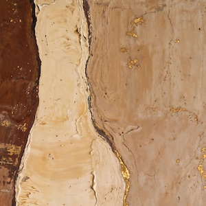 May include: An abstract painting featuring vertical bands of deep burgundy, creamy beige, and light tan. The sections are separated by thin, textured lines of metallic gold leaf, with additional gold leaf accents scattered across the surface.