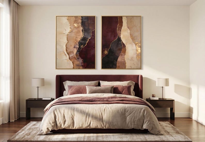 May include: Two rectangular wall art pieces featuring abstract vertical layers of cream, tan, deep burgundy, and black paint with metallic gold accents, displayed in thin gold frames above a dark burgundy upholstered bed with neutral bedding.
