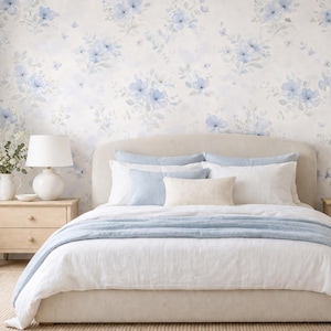 Peut inclure: Intérieur de chambre à coucher avec un lit aux draps blancs et des coussins bleus clairs. Le mur est orné d'un papier peint floral bleu et blanc. Deux tables de chevet en bois avec des lampes sont de chaque côté du lit.