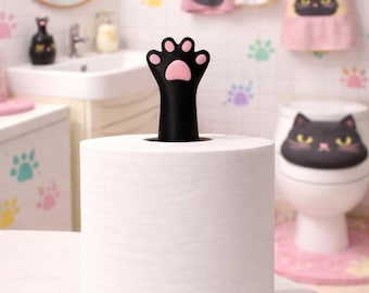 May include: A white paper towel roll with a black base and a black cat paw-shaped topper with a pink paw pad. The bathroom setting includes cat-themed decor like towels and a toilet seat cover.