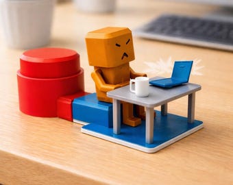 May include: A small orange box-shaped figure with an angry expression sits at a gray desk with a white mug and a blue laptop. The figure is positioned on a blue platform connected to a red cylindrical base, creating a miniature office scene.