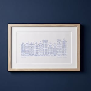 May include: A framed print featuring a blue line drawing of Amsterdam canal houses. The artwork is set against a white background, encased in a light wood frame. The print includes text at the bottom.