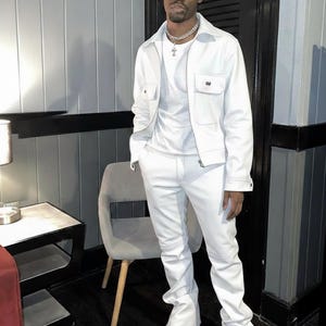 Puede incluir: Un atuendo blanco que consta de una chaqueta con dos bolsillos en el pecho, una camiseta y pantalones. El atuendo se combina con botas blancas con suelas gruesas y un collar plateado.