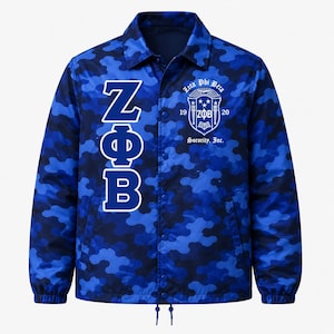 May include: A blue camouflage print coach jacket featuring a snap-button front closure, a collar, and long sleeves with elastic cuffs. The front displays the Greek letters ZΦB vertically in white and a white Zeta Phi Beta Sorority, Inc. crest logo.