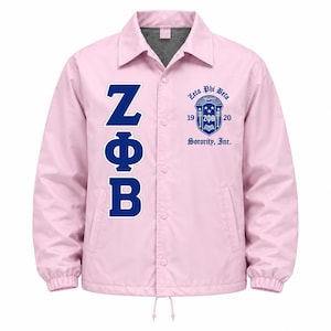 May include: A light pink snap-front jacket featuring the dark blue Greek letters ZΦB vertically on the left side and a dark blue Zeta Phi Beta Sorority, Inc. crest with the years 1920 on the right chest, complete with a collar and elastic cuffs.