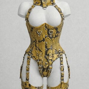 Peut inclure: Un corset jaune et noir à motif peau de serpent, avec un col halter, des éléments métalliques et des jarretières. Le corset est présenté sur un mannequin blanc, mettant en valeur son design ajusté et ses détails complexes.