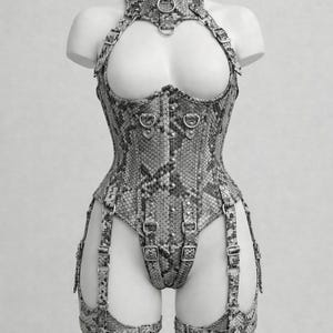 Peut inclure: Un corset à motif peau de serpent avec un col montant, des bretelles et des jarretelles attachées. Le corset comporte des détails d'anneaux et de boucles en métal. Le vêtement est présenté sur un mannequin.