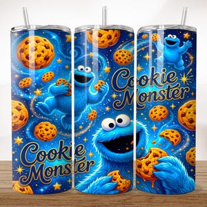 May include: A cylindrical tumbler featuring a blue, starry space background with multiple chocolate chip cookies and the blue Cookie Monster character. The text Cookie Monster is printed in a gold script font. The tumbler includes a clear plastic straw.