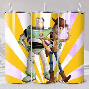 May include: A cylindrical stainless steel tumbler with a clear lid and straw, featuring a vibrant yellow and white sunburst background pattern. The design displays the characters Buzz Lightyear and Woody from Toy Story standing side by side.