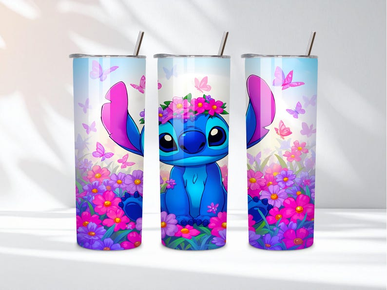 May include: Three cylindrical tumblers with metal straws featuring a blue alien character with large ears wearing a pink flower crown. The design includes a vibrant field of pink, purple, and magenta flowers with scattered pink butterflies against a light blue sky.