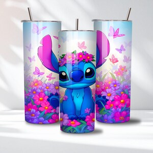May include: Three cylindrical stainless steel tumblers with metal straws, featuring a blue alien character wearing a pink flower crown, surrounded by vibrant pink and purple flowers and butterflies against a light blue and white gradient background.