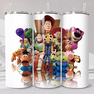 May include: A white cylindrical tumbler with a clear lid and straw, featuring a colorful graphic print of various Toy Story characters including Woody, Buzz Lightyear, Jessie, Mr. Potato Head, Rex, and Lotso against a white background.