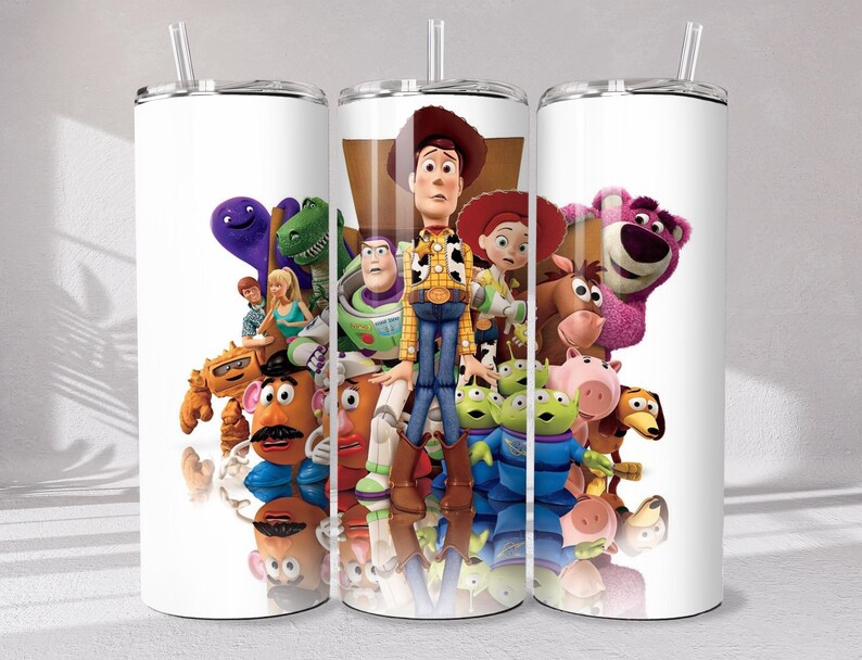 May include: A white cylindrical tumbler with a clear lid and straw, featuring a colorful graphic print of various Toy Story characters including Woody, Buzz Lightyear, Jessie, Mr. Potato Head, Rex, and Lotso against a white background.