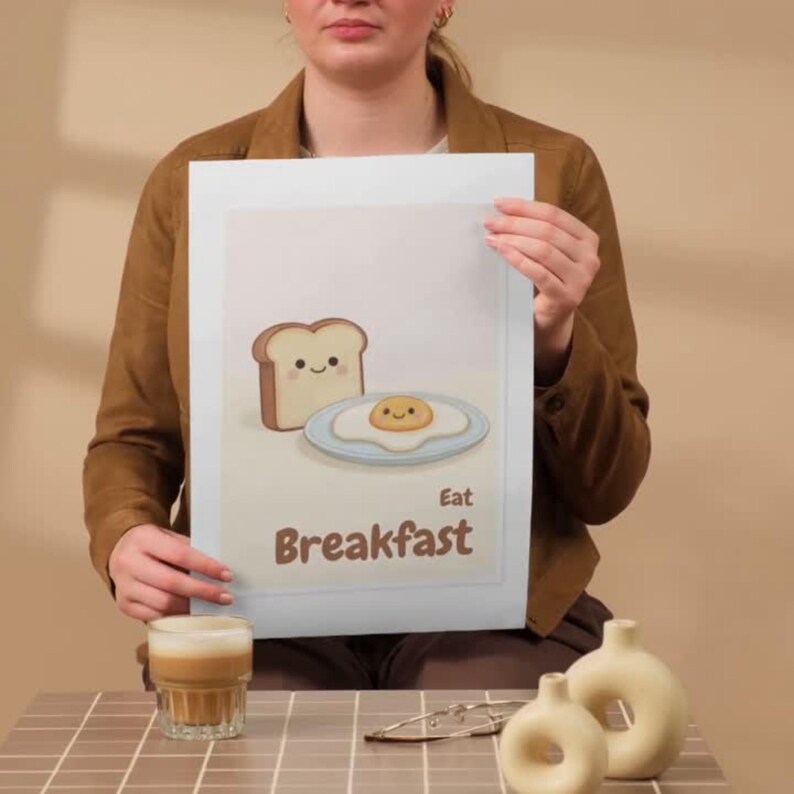 Pode incluir: Uma impress&atilde;o com uma ilustra&ccedil;&atilde;o de desenho animado de caf&eacute; da manh&atilde;. A imagem inclui uma fatia de p&atilde;o e um ovo frito com rostos sorridentes. As palavras "Eat Breakfast" est&atilde;o escritas em texto marrom abaixo.