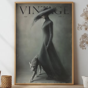 May include: Vintage magazine cover print featuring a woman in a long dress and hat, walking with a leopard. The print has a muted color palette with the word "VINTAGE" at the top, and the year "1951". The print is framed in a wooden frame.