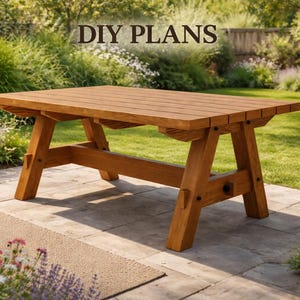 May include: A rectangular wooden picnic table with a slatted top and A-frame legs, featuring the text DIY PLANS centered above it. The table is constructed from light brown wood planks and is positioned on a stone patio in an outdoor setting.